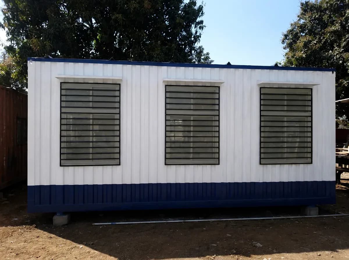 Illustrative example of the long side of a white and blue container office cabin, with three windows fitted with grilles