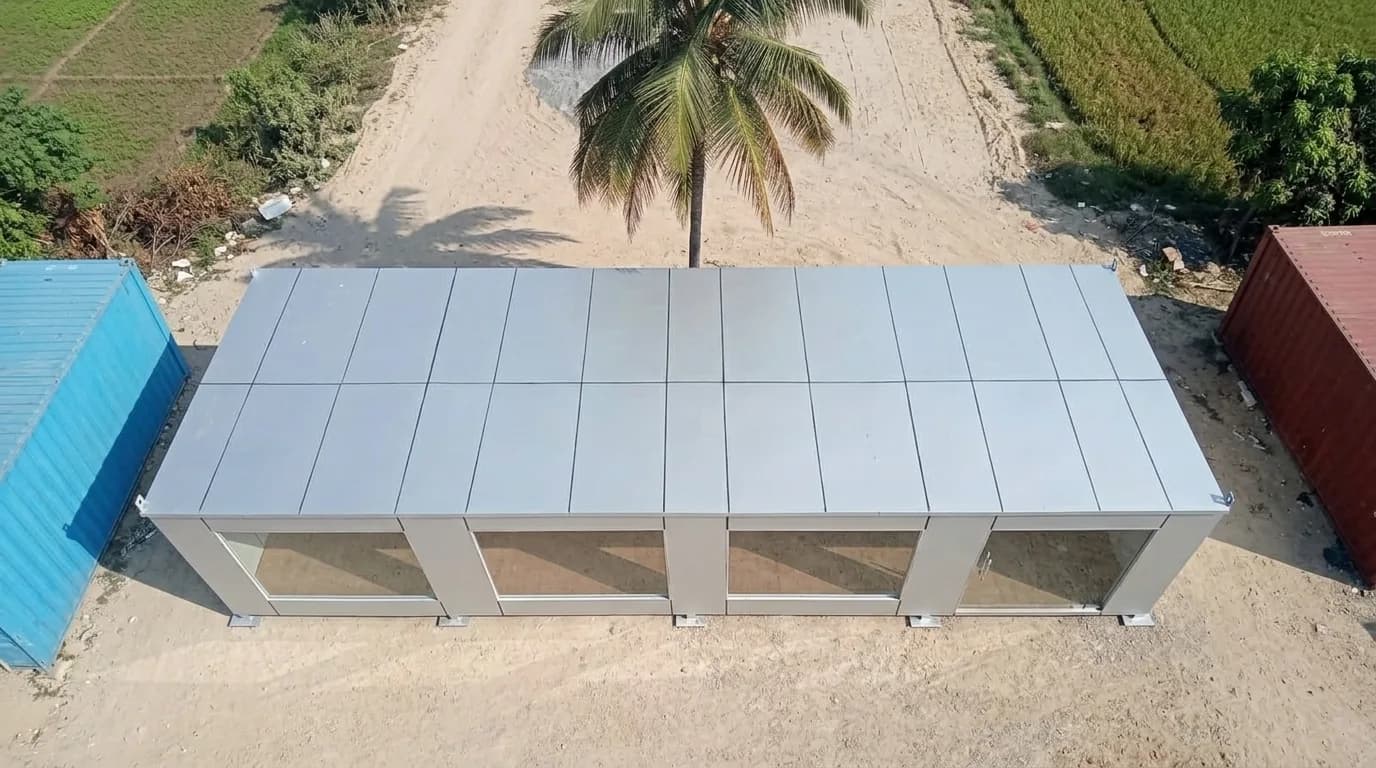 Container office near Tata Electronics, Hosur — drone view of the flat-roof glass-front unit standing between shipping containers in the vendor yard