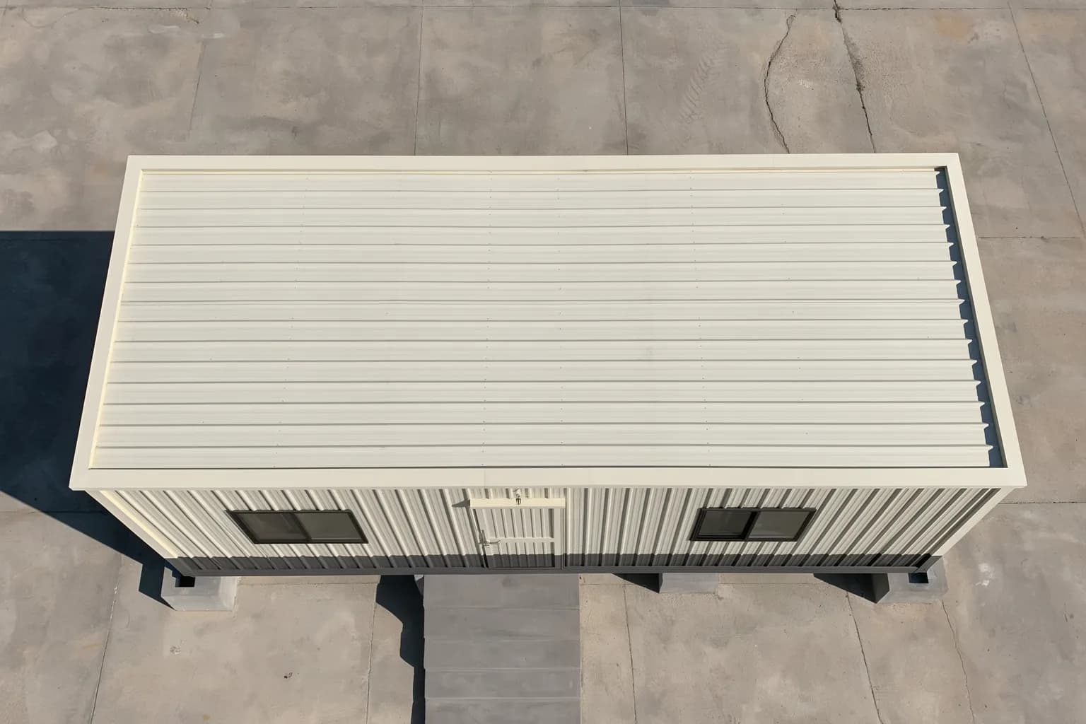 Portable cabin in Kolar — illustrative top-down view of the cream ribbed-steel cabin roof, its door-side windows and the stair, on a paved yard