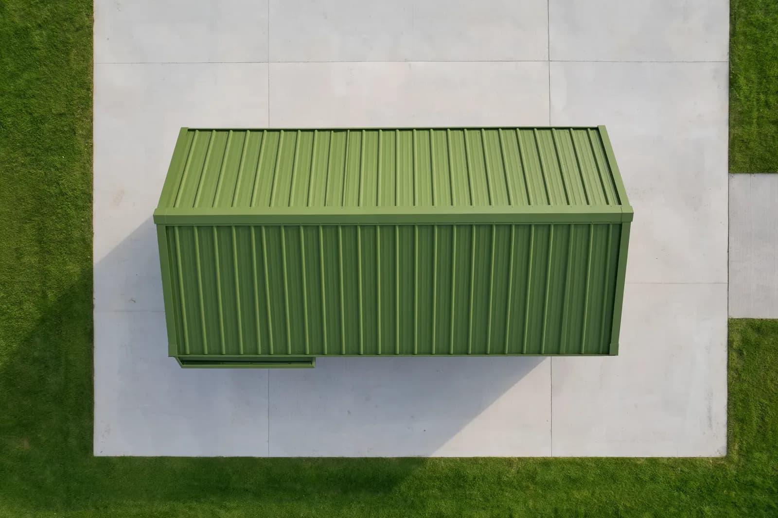 Portable cabin in Magadi — illustrative aerial view of the olive-green cabin's corrugated roof and door hood, placed on a concrete pad surrounded by lawn