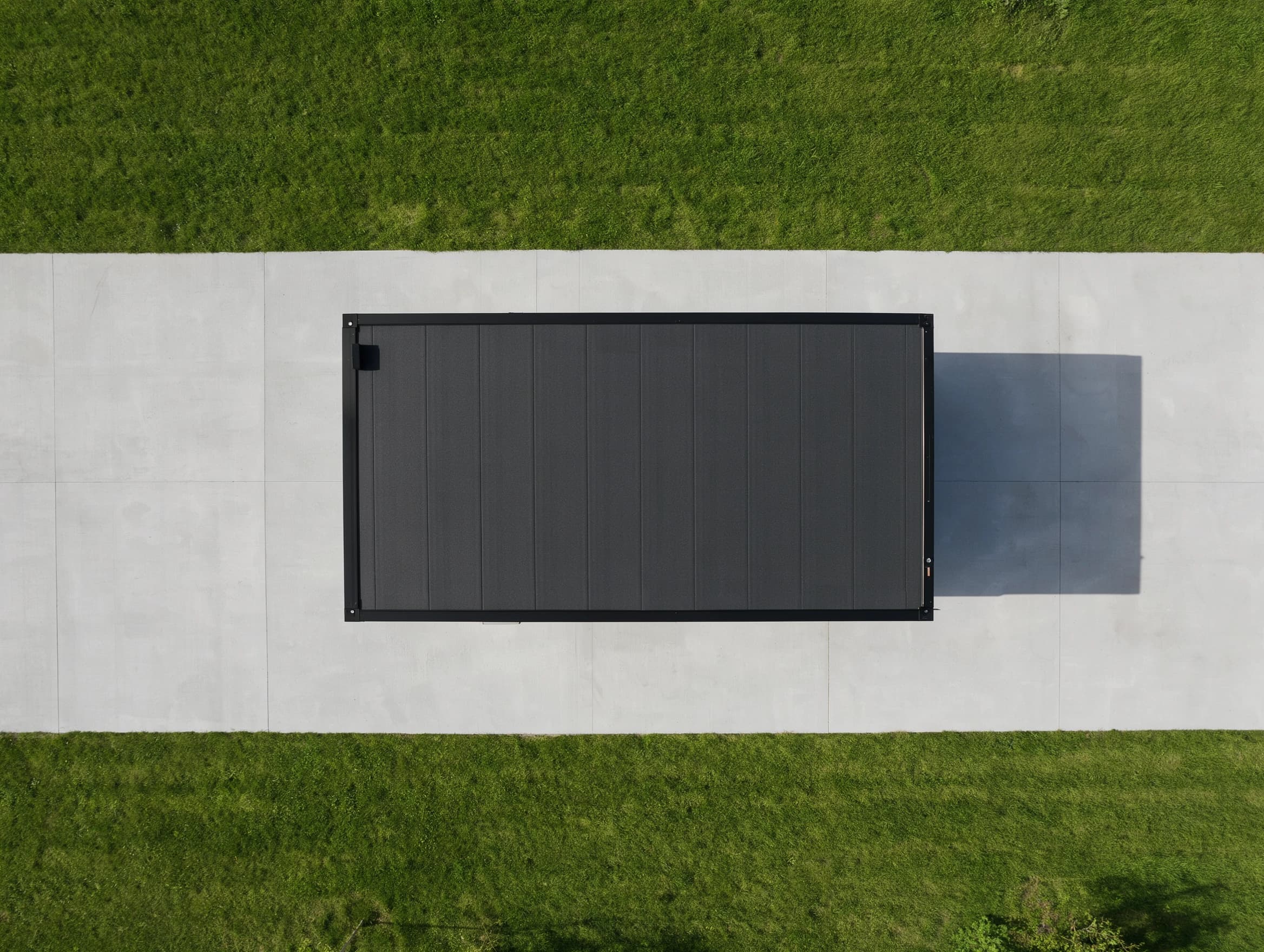 Portable cabin in Machenahalli Industrial Area, Shivamogga — illustrative top-down render of the cabin's dark panelled roof inside its black edge frame, standing on a concrete strip between two lawns