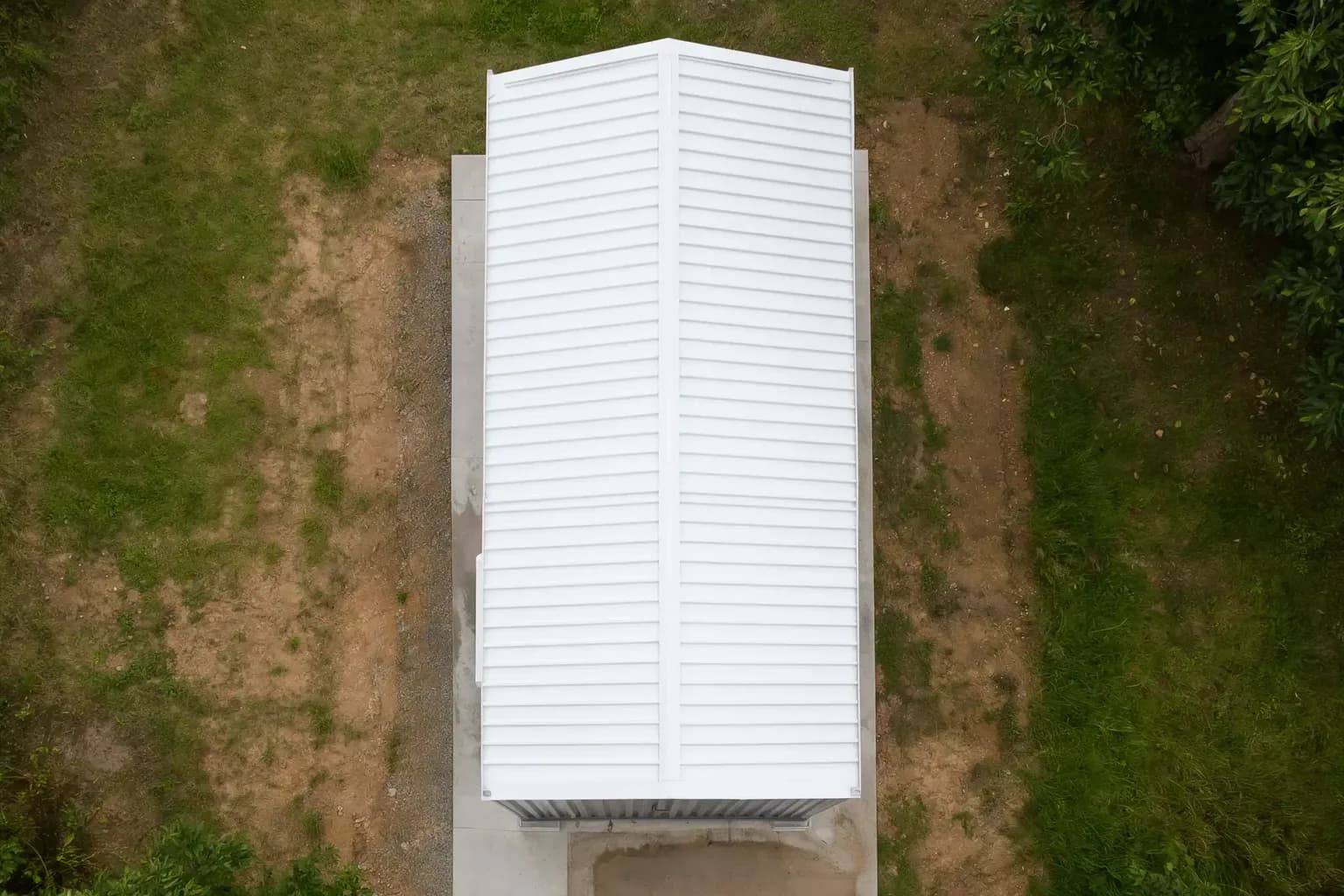 Portable cabin for Tindivanam and SIPCOT Industrial Park sites — illustrative top-down view of the cabin's white gabled roof on a concrete pad, with grass and trees around the plot