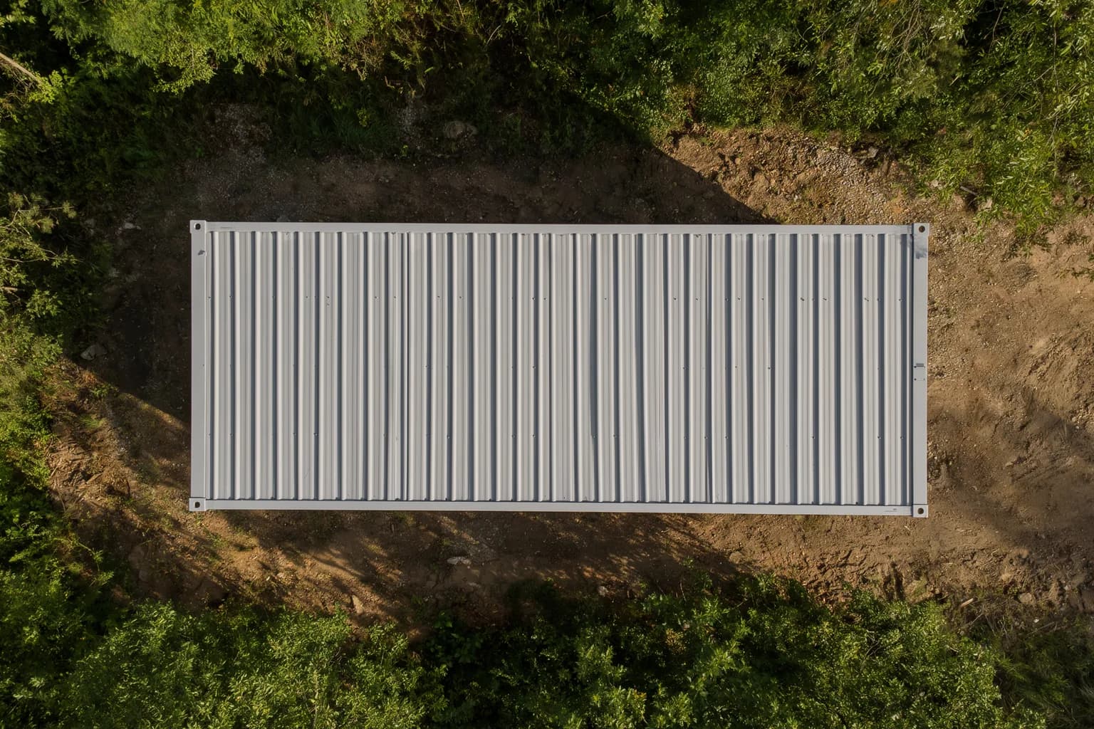 Portable cabin in Tiruvallur — illustrative top-down view of the cabin's grey corrugated roof and corner castings, on a cleared plot surrounded by vegetation