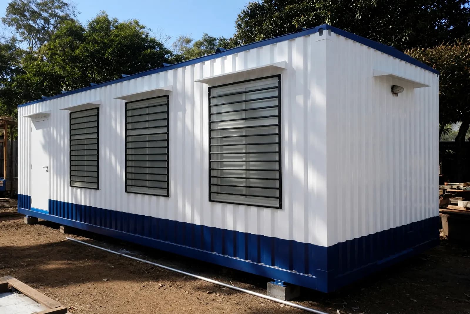 Illustrative example of a white and blue container office cabin with a door and three windows fitted with grilles Illustrative example of a white and blue container office cabin with a door and three windows fitted with grilles